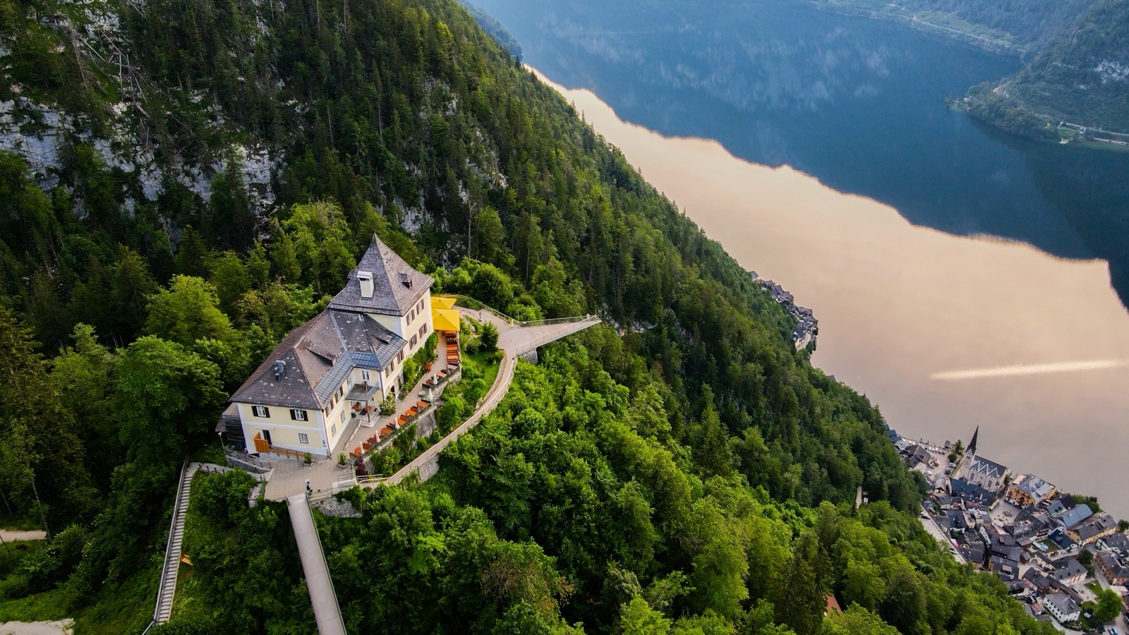 Vista aérea de un edificio y una pasarela sobre un espolón boscoso muy por encima del lago y los tejados de Hallstatt