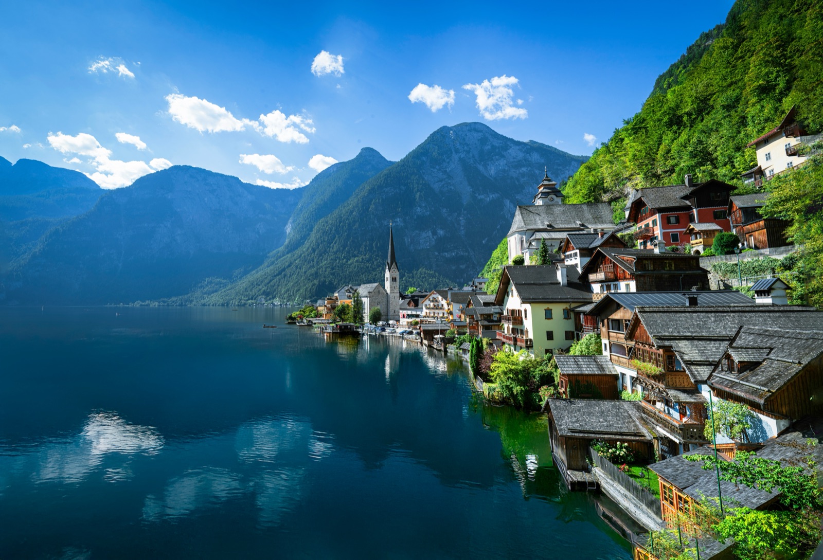 Wooden houses of Hallstatt on a steep slope above the lake, with a church spire and mountains reflected in calm water